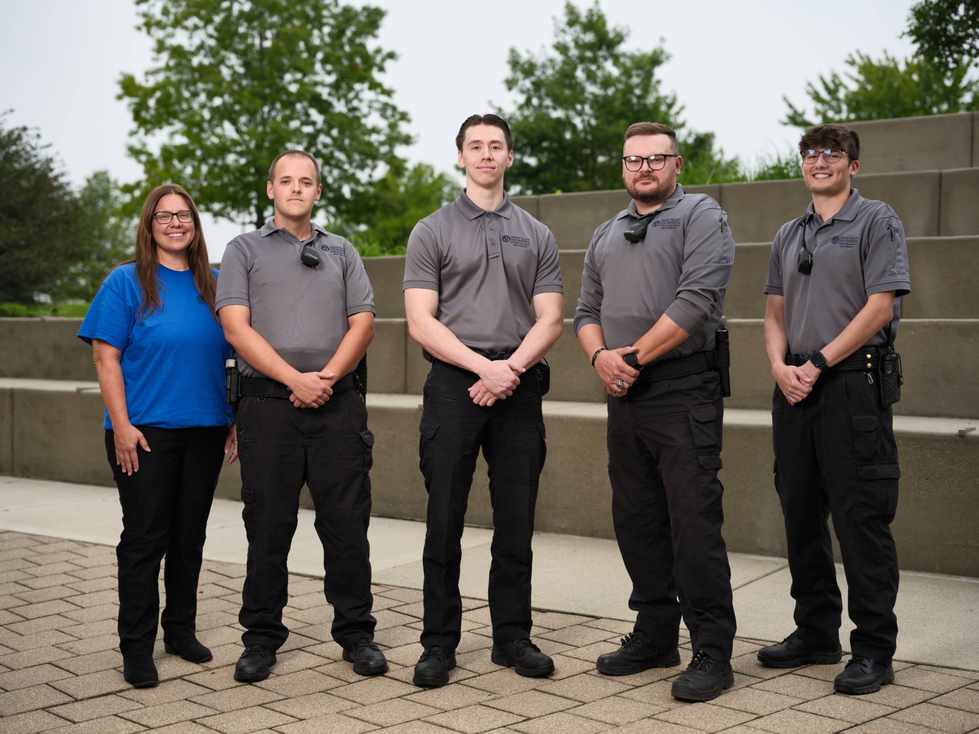 Security employees, 4 in uniform, and 1 supervisor in plain clothes, posing in front of the Student Services fountain. Subjects are smiling.